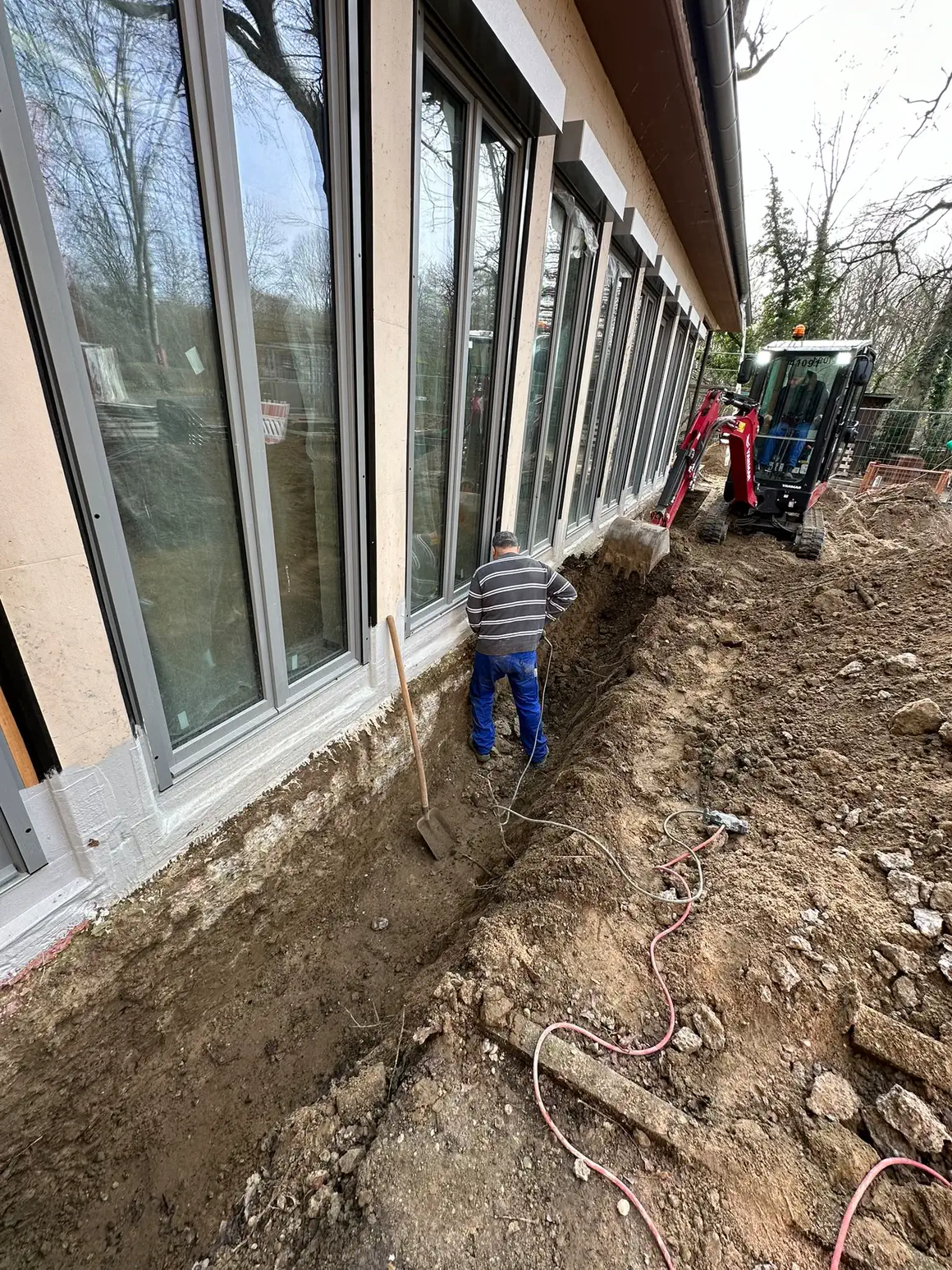 Mitarbeiter von Bodin Bau beim Aushub von Hand unter dem Fensterband, dahinter der Minibagger